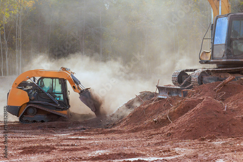 Two construction machines dig move dirt at work site with dust rising in air