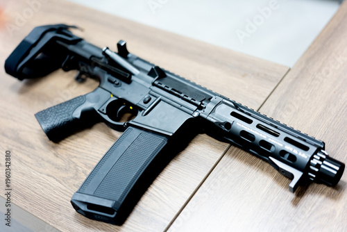 Slika na platnu Black tactical rifle with collapsible stock resting on wooden surface in urban s