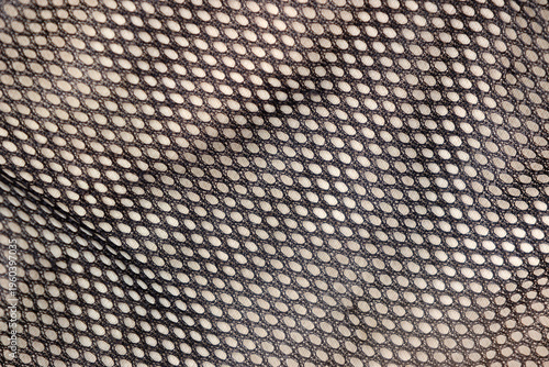 Close-up of black mesh fabric with uniform oval perforations and soft folds creating a textured pattern