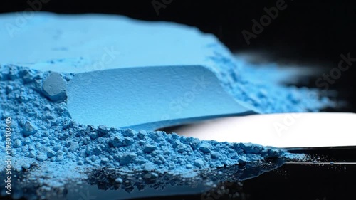Powdered blue pigment on a shiny metallic scoop with fine crumbs and smeared edge