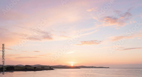 Beautiful sunset over calm sea horizon with soft pastel sky and distant hills, peaceful coastal landscape scene in natural evening light.