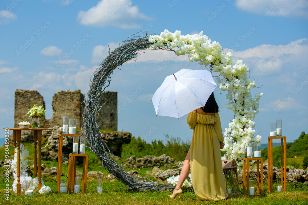 Fototapeta premium Elegant bride woman under wedding arch. Romantic wedding arch outdoor scene. Bride under floral wedding decor. Luxury wedding arch with flowers. Beauty bride ceremony concept.