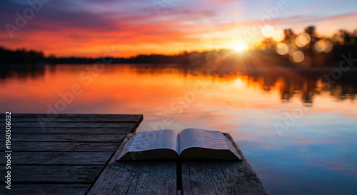 Open book lying on wooden dock at beautiful tranquil sunset lake perfect for peaceful spiritual reading concept and quiet inspiring retreat