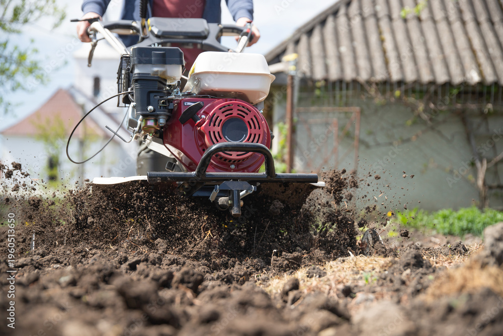 Fototapeta premium Farmer using tiller on a plowed field