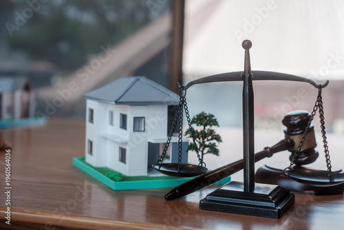 Legal concept still life with scale of justice and gavel beside miniature house model on desk, symbolizing real estate law, property rights, mortgage, court decision, and litigation.