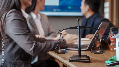 Legal consultation meeting with lawyers in office, focus on balance scales on desk, justice and contract concept with blurred professionals in background.