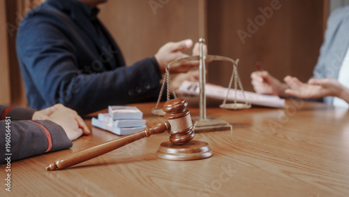 Fotografie Close-up of legal consultation meeting with attorneys at desk, scales of justice and gavel in focus, paperwork in foreground, warm office light