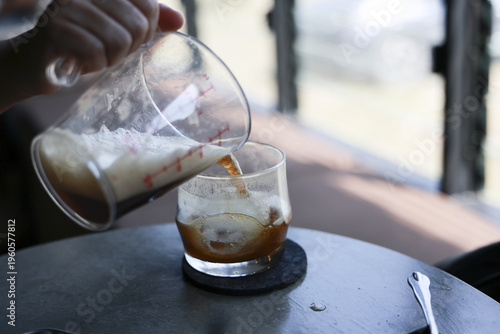 Hand pour cold coffee espresso into glass of milk on cafe table creating delicious refreshing morning drink while barista feeling calm and focused working in natural daylight