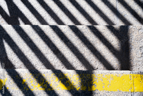 Staircase with shadows, a yellow stripe on the first step as a warning sign, sunny day 