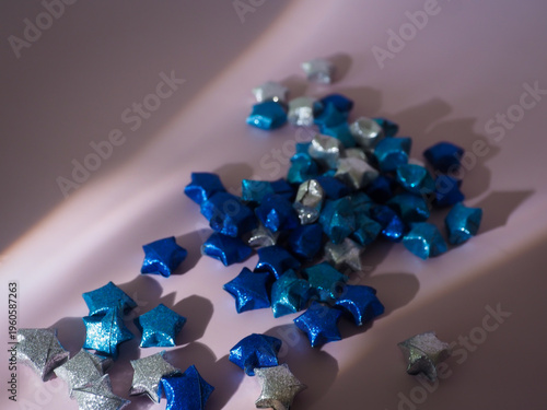 Top view of blue paper stars on a pastel backdrop featuring artistic light play. High-quality aesthetic background for greeting cards, social media posts, and modern stationary branding.