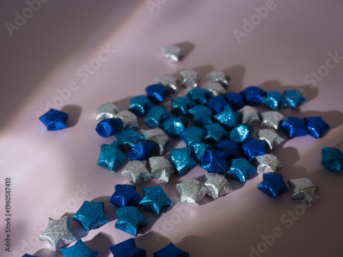 Top view of blue paper stars on a pastel backdrop featuring artistic light play. High-quality aesthetic background for greeting cards, social media posts, and modern stationary branding.