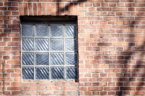 Red brick wall with glas brick window, sunny day, shadows on the wall,  old bricks with rough surface, no person