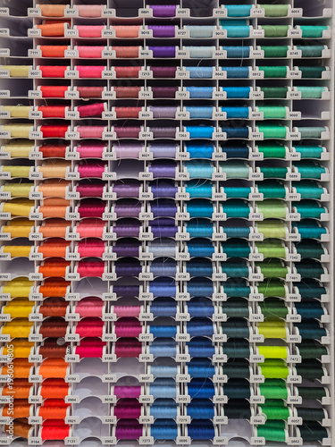 Multi-colored sewing threads on shop window. Hobby and needlework shop with collection of threads. Colored spools of threads. Vertical full frame background