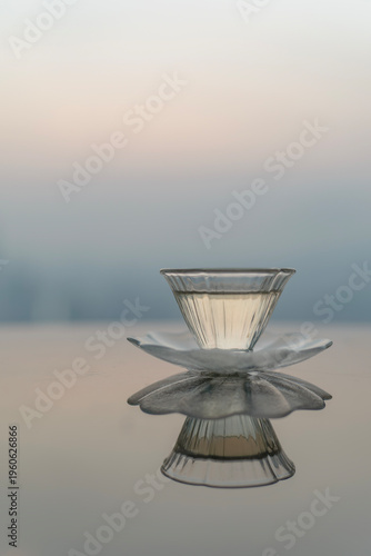 Flower-shaped glass tea cup on reflective table with city skyline