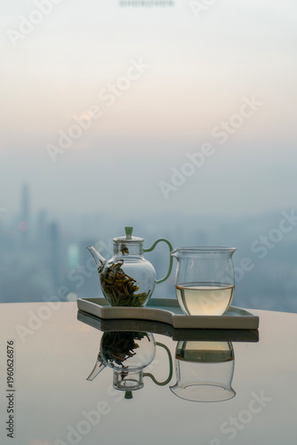 Glass teapot and fair cup on reflective table with city skyline