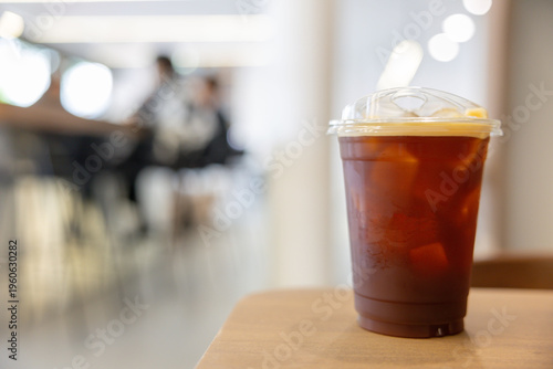 Iced coffee in clear plastic cup with lid, resting on wooden surface