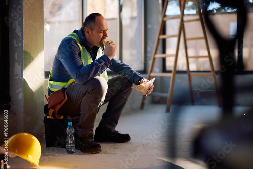 Mature worker enjoying in sandwich on lunch break at construction site.