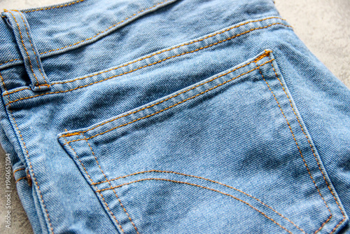 Close-up of a denim jeans back pocket with double orange stitching, showing detailed fabric texture and classic blue jean material. Casual fashion fabric