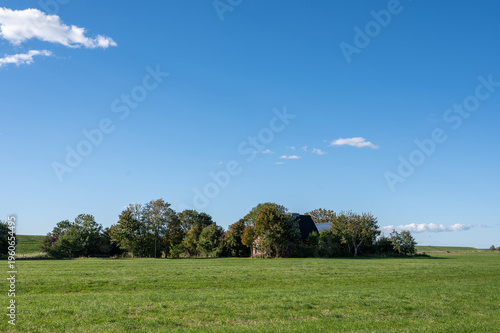 A house surrounded by green trees, on a dike on the North Sea coast