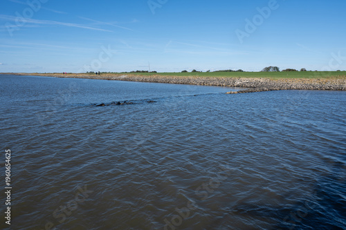 View from the North Sea towards the coast with stone wall, meadow and some trees