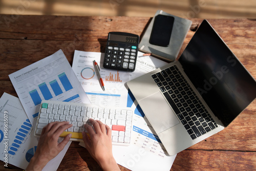 Fotografie Person working on a wooden desk, analyzing financial data and charts on multiple