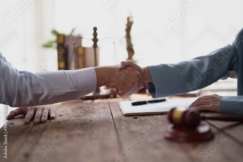 Two business people or legal professionals shaking hands across a wooden table, emphasizing successful agreement, partnership, and resolution in a legal or corporate setting