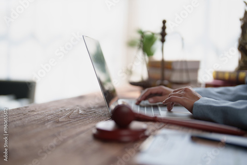 Legal professional hands typing on a laptop, conducting research in a law office or courtroom setting, with a gavel and balance scale symbolizing justice and legal practice