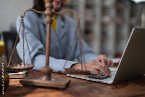 Professional lawyer or attorney researching legal cases and providing advice while typing on a laptop with the symbolic scales of justice on a wooden desk in an office