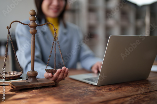Person working on a laptop at a wooden desk with a justice scale, symbolizing modern legal practices, online consultation, legal advice, and the concept of balance and equity in law