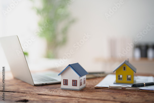 Εκτύπωση καμβά Two miniature houses on a rustic wooden desk beside an open laptop and clipboard