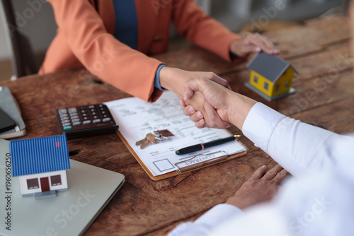 Fotografie Business professionals shaking hands over a wooden table with house models, keys