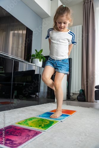 Little girl stepping and jumping on colorful sensory gel mats placed on floor at home. Sensory development, autism support and occupational therapy activity concept.