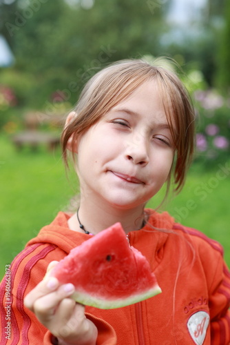 A girl in nature eats a red watermelon and smiles. Happy girl eating watermelon in nature