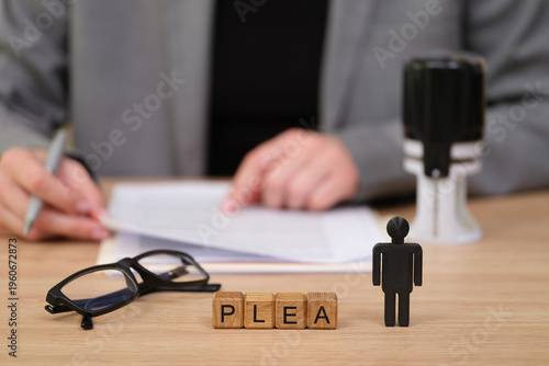 Tableau sur toile A focused individual reviews documents in a legal setting, highlighting a plea made evident by wooden blocks