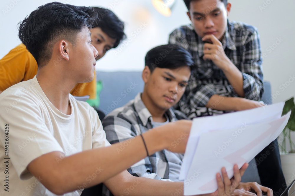 Fototapeta premium Four Young Asian Men Discussing Paperwork and Collaborating on Project in Bright Indoor Setting