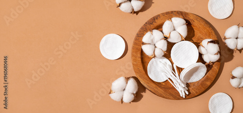 Natural cotton pads, cotton swabs and lush cotton flowers on wooden tray on brown background. Beauty, health and personal care concept. Cosmetic accessories for makeup removal and facial care