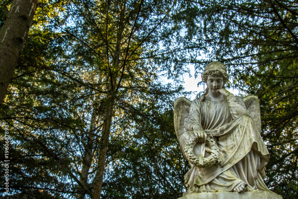 Naklejka premium Pensive Winged Angel Statue Under Trees