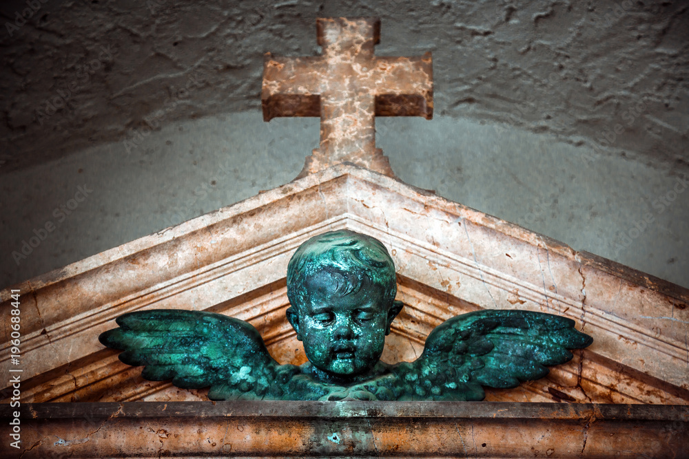 Naklejka premium Winged Cherub Statue Below Stone Cross