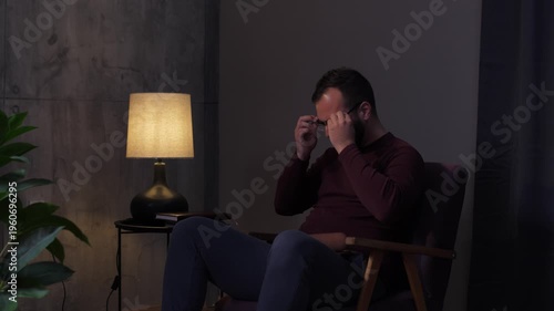Bearded man putting on glasses and reading a book at night
