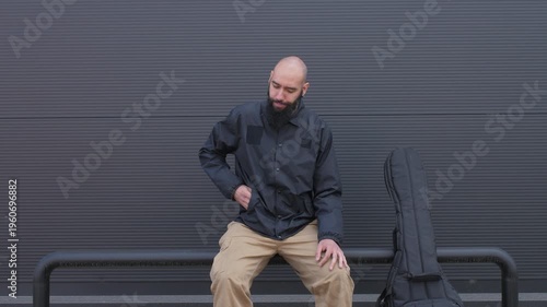Bald bearded musician sitting and using smartphone