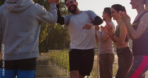 Happy athletes of fitness team celebrate goal achievement and triumph of marathon runner in summer park. People applaud running winner, give high five to man after race and success of run outdoor