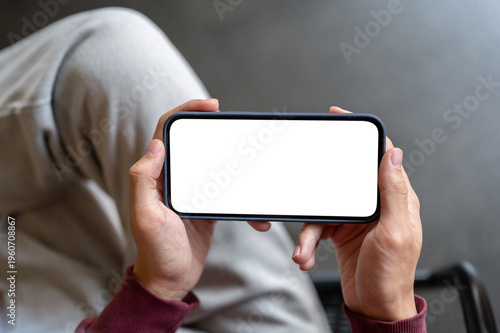 Top view of a man's hands holding white screen phone watching videos while sitting on chair in cafe.