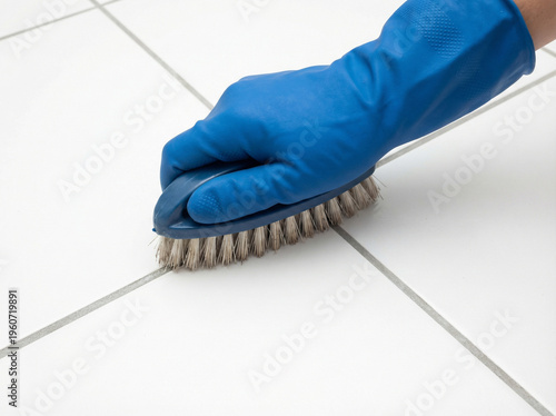 Close up of hand wearing blue protective glove scrubbing tile floor with brush, highlighting cleaning, hygiene, sanitation, home maintenance, disinfecting surfaces and deep grout cleaning routine