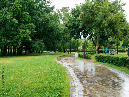 Bild auf Leinwand Wet curved cobblestone path in a park after rain with green grass and trees, ref