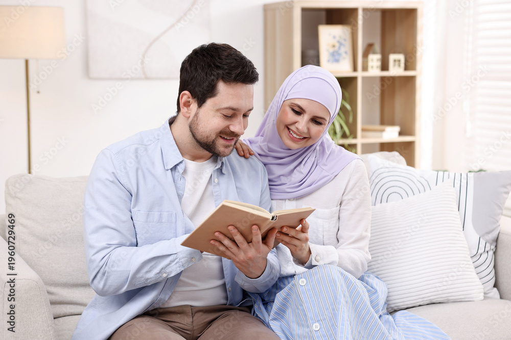 Fototapeta premium Happy muslim couple reading book on sofa at home