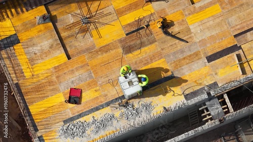 Aerial drone shot looking straight down at two construction workers installing steel reinforcement on formwork deck, showcasing structural preparation and active building process.
