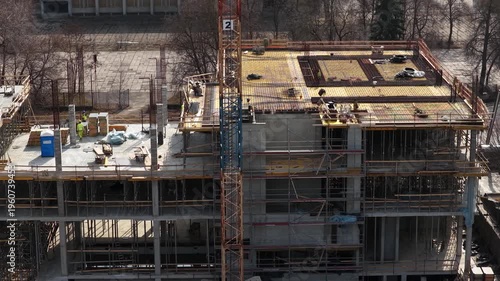 Drone footage capturing a partially completed multi story concrete building with scaffolding, formwork, and materials, highlighting structural progress and active construction environment.