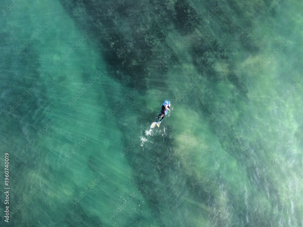 Fototapeta premium An explorer on a surfboard rests amidst the vast ocean, capturing the peaceful and adventurous spirit of surfing surrounded by the mesmerizing beauty of blue waters.