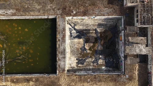 Top-down drone shot of derelict industrial area featuring empty concrete basins, stagnant water, debris, and weathered surfaces, illustrating decay, neglect, and urban abandonment.