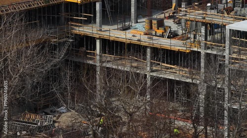 Drone footage capturing a partially completed multi story concrete building with scaffolding, formwork, and materials, highlighting structural progress and active construction environment.